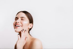 woman uses skincare and moisturizer in her face while smiling